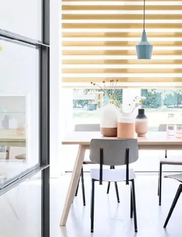 Okergeel duo-rolgordijn voor het raam van een lichte eetkamer.
