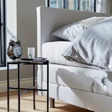 Bed met hoofdkussens naast een nachtkastje met wekker.
