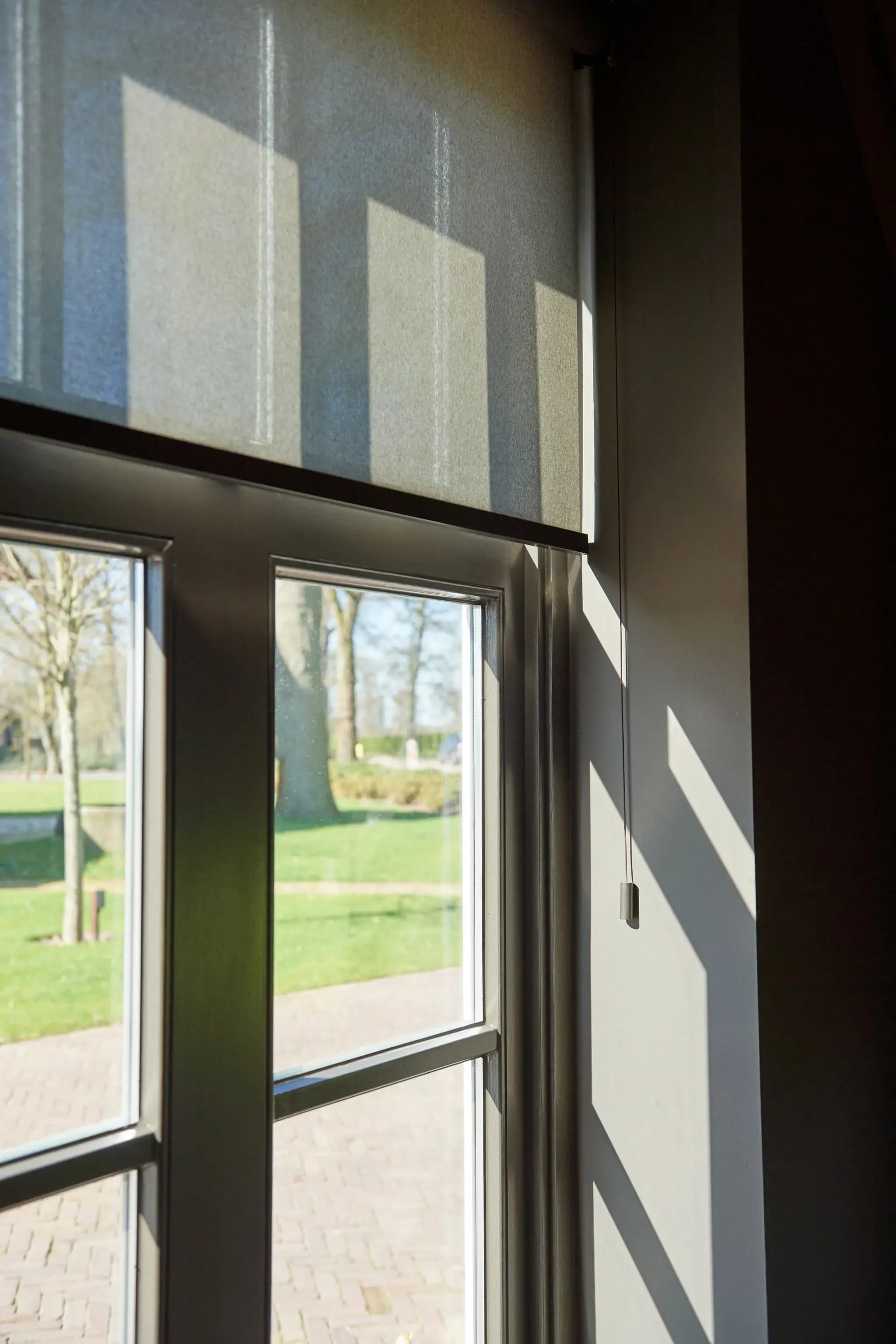 Rolgordijnen voor een groot raam met uitzicht op de tuin.