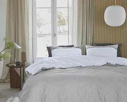 Bed met een zandkleurig dekbedovertrek in een lichte slaapkamer.