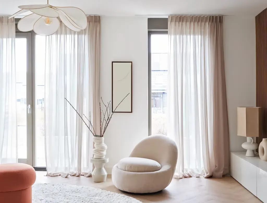 Lichte inbetweens voor de ramen van een zitkamer met een ronde fauteuil.
