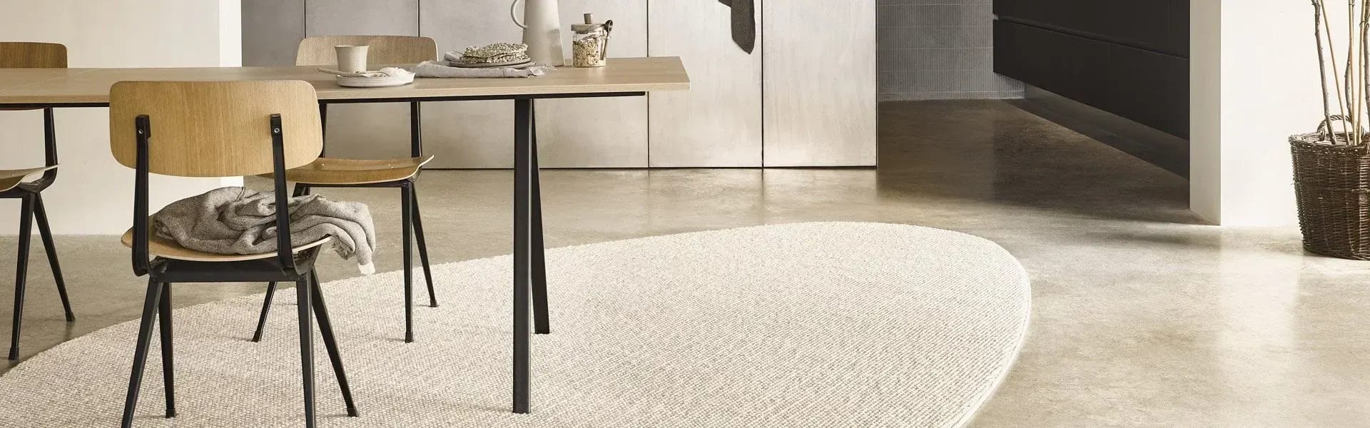 Licht karpet onder een eettafel op een betonvloer.