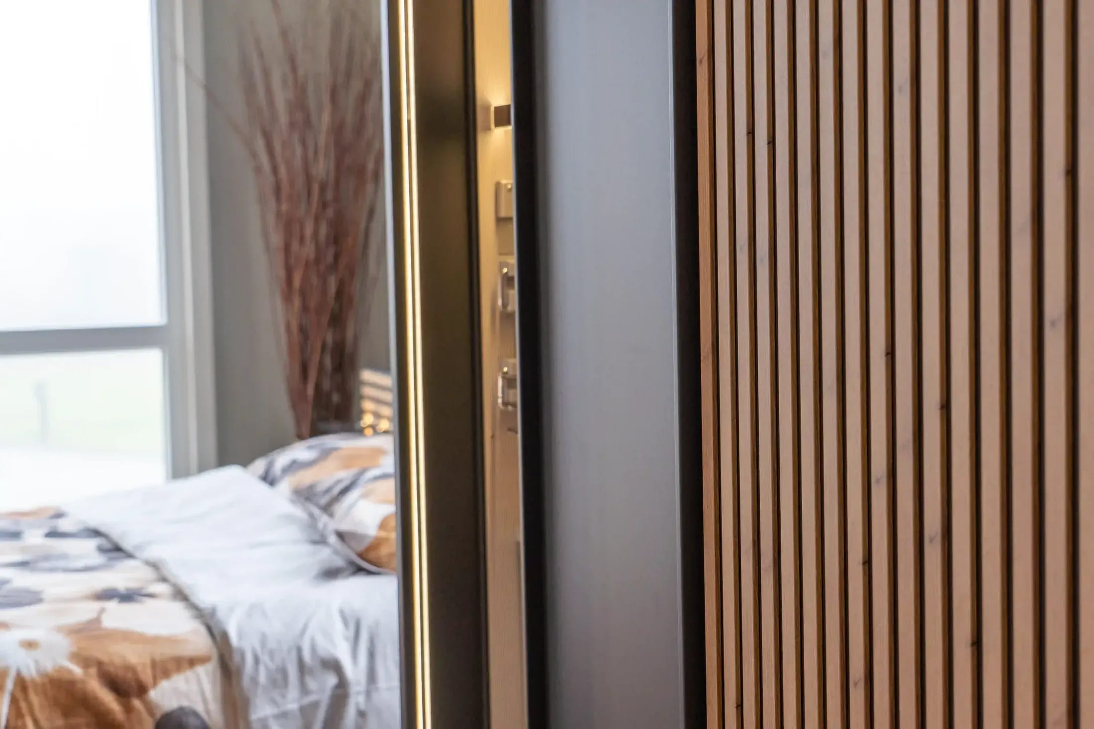 Detail van een donkere kastwand met verticale houten latten naast een opgemaakt bed.
