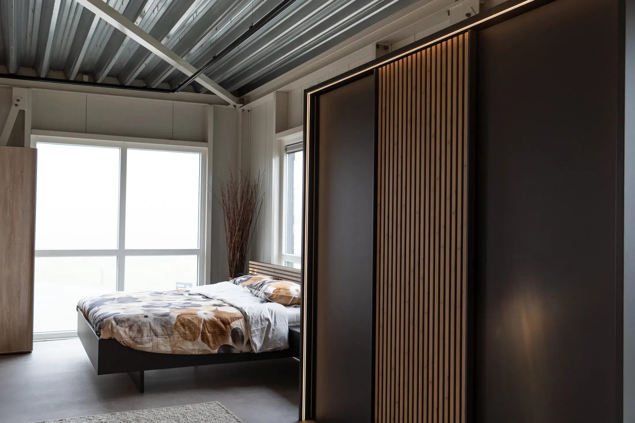Kastwand met schuifdeuren en houten latten in een slaapkamer met groot raam.