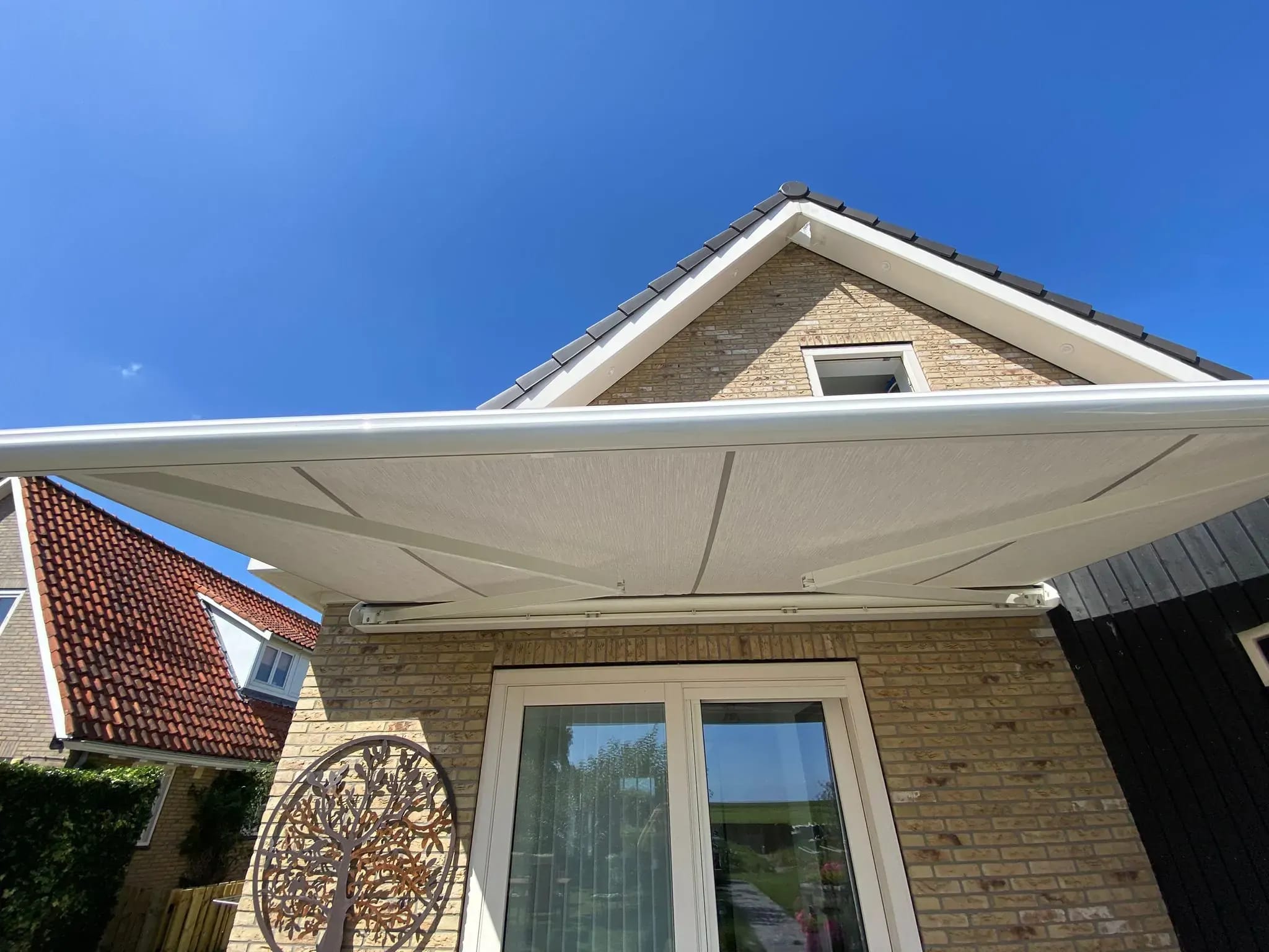 Het doek van een knikarmscherm boven de tuindeuren van een woning op Terschelling.