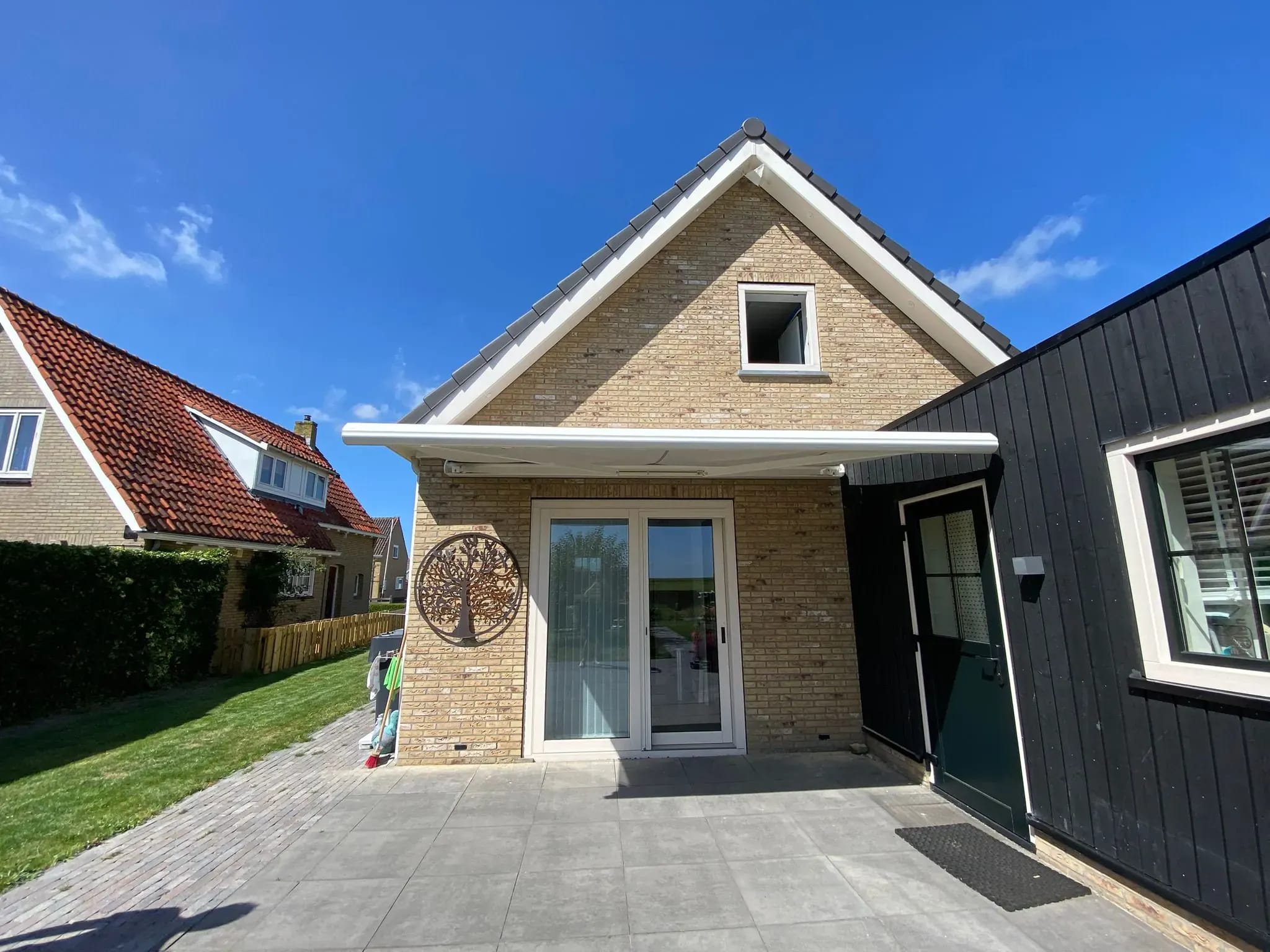 Knikarmscherm half uitgeklapt boven het terras van een woning op Terschelling.