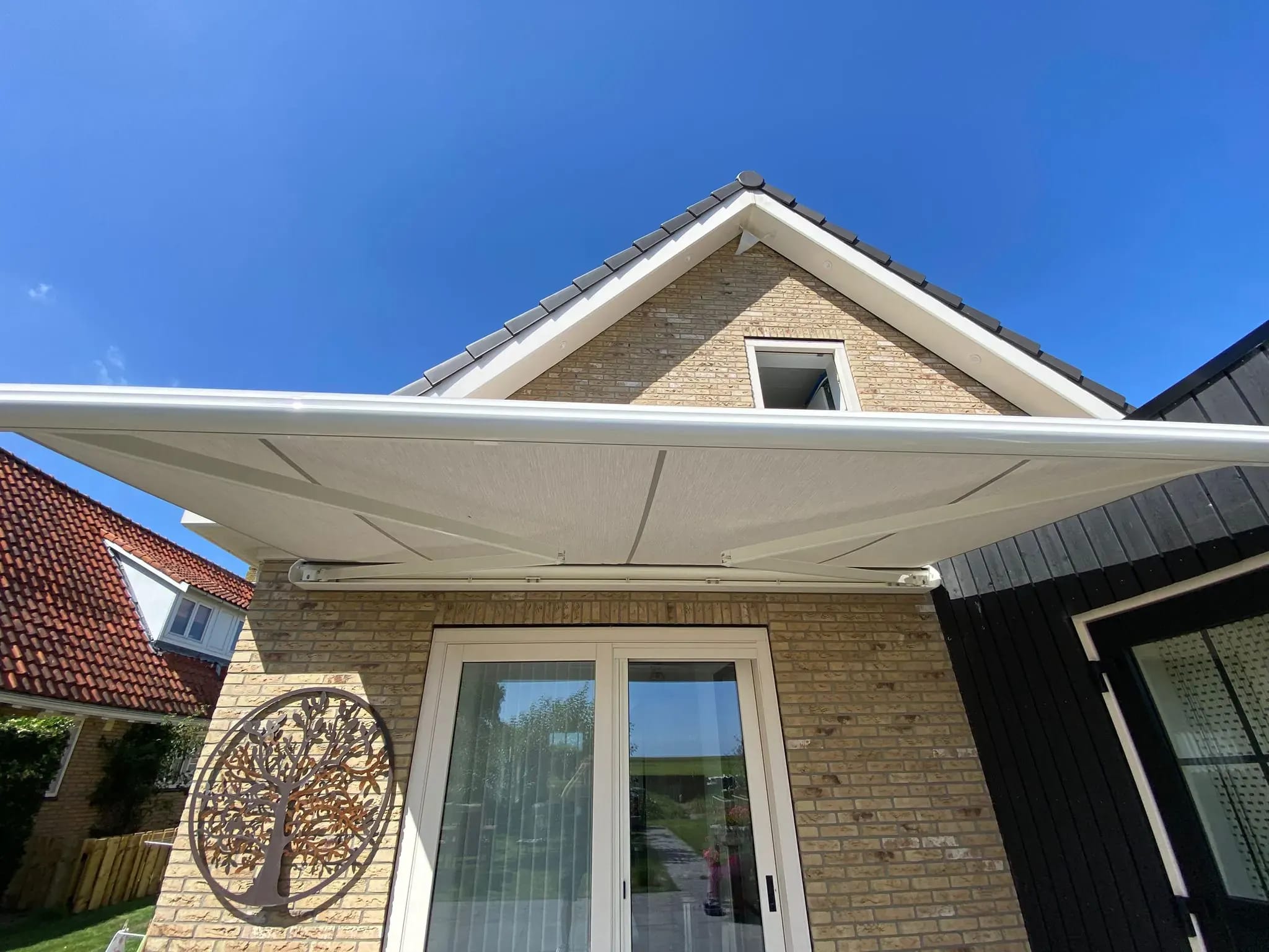Wit knikarmscherm uitgeklapt boven de terrasdeuren, van onderaf gezien.
