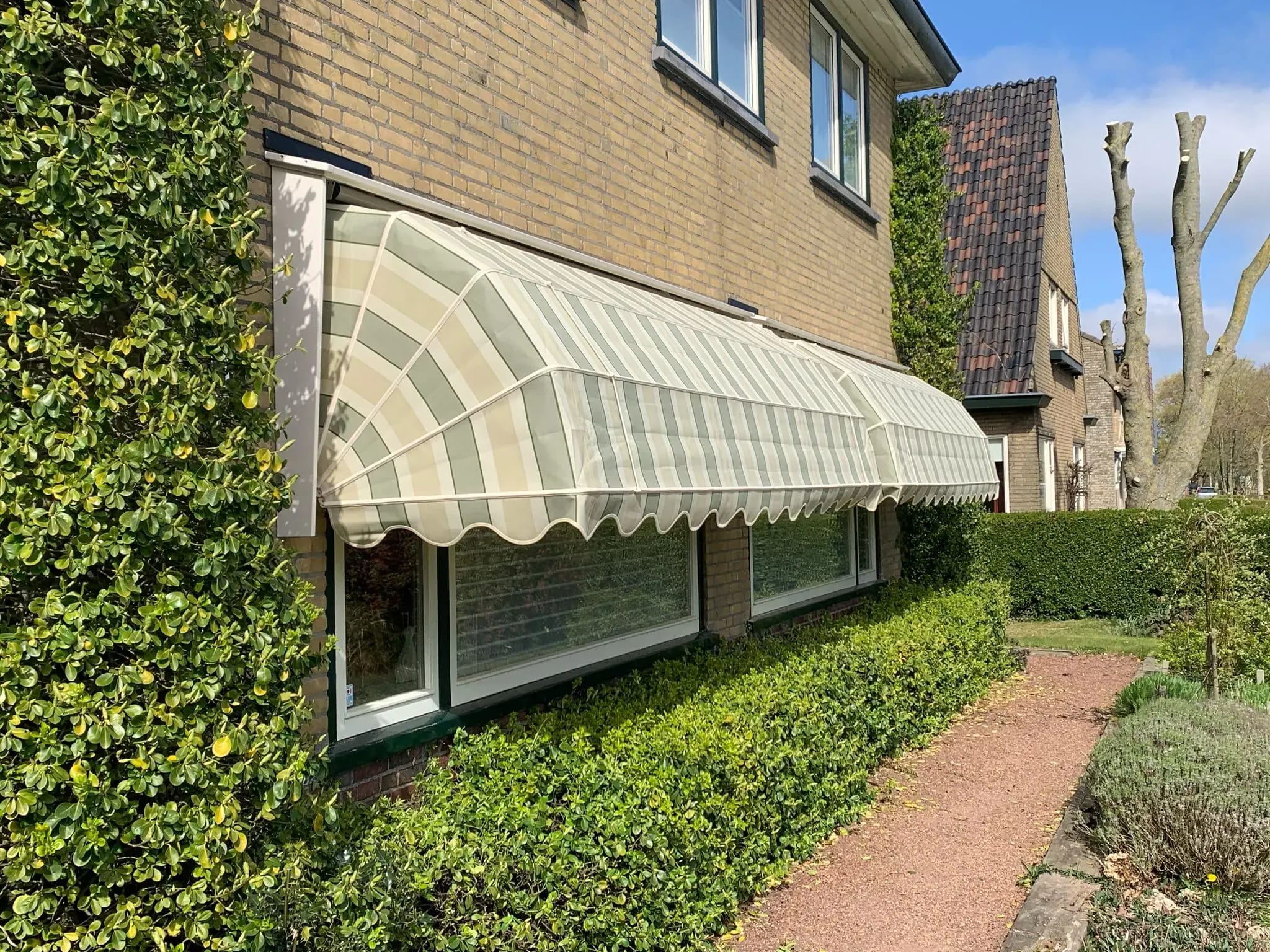 Groen-wit gestreepte markiezen boven de ramen van een bakstenen woning.