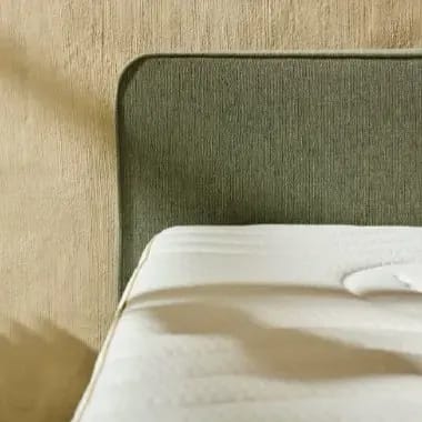 Detail van de gewatteerde tijk van een matras bij een groen hoofdbord.