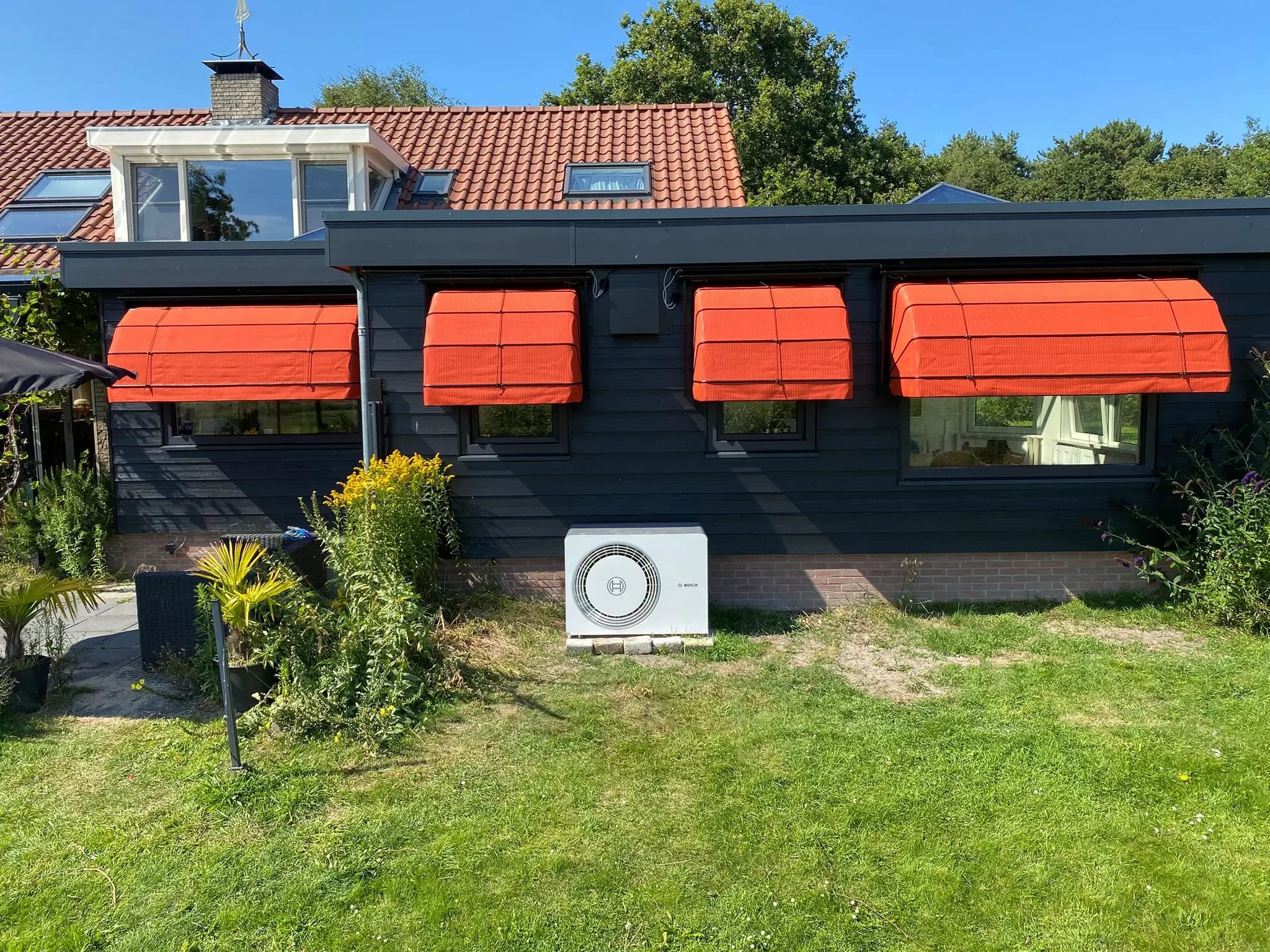 Oranje markiezen voor de ramen van een donkere houten gevel op Terschelling.