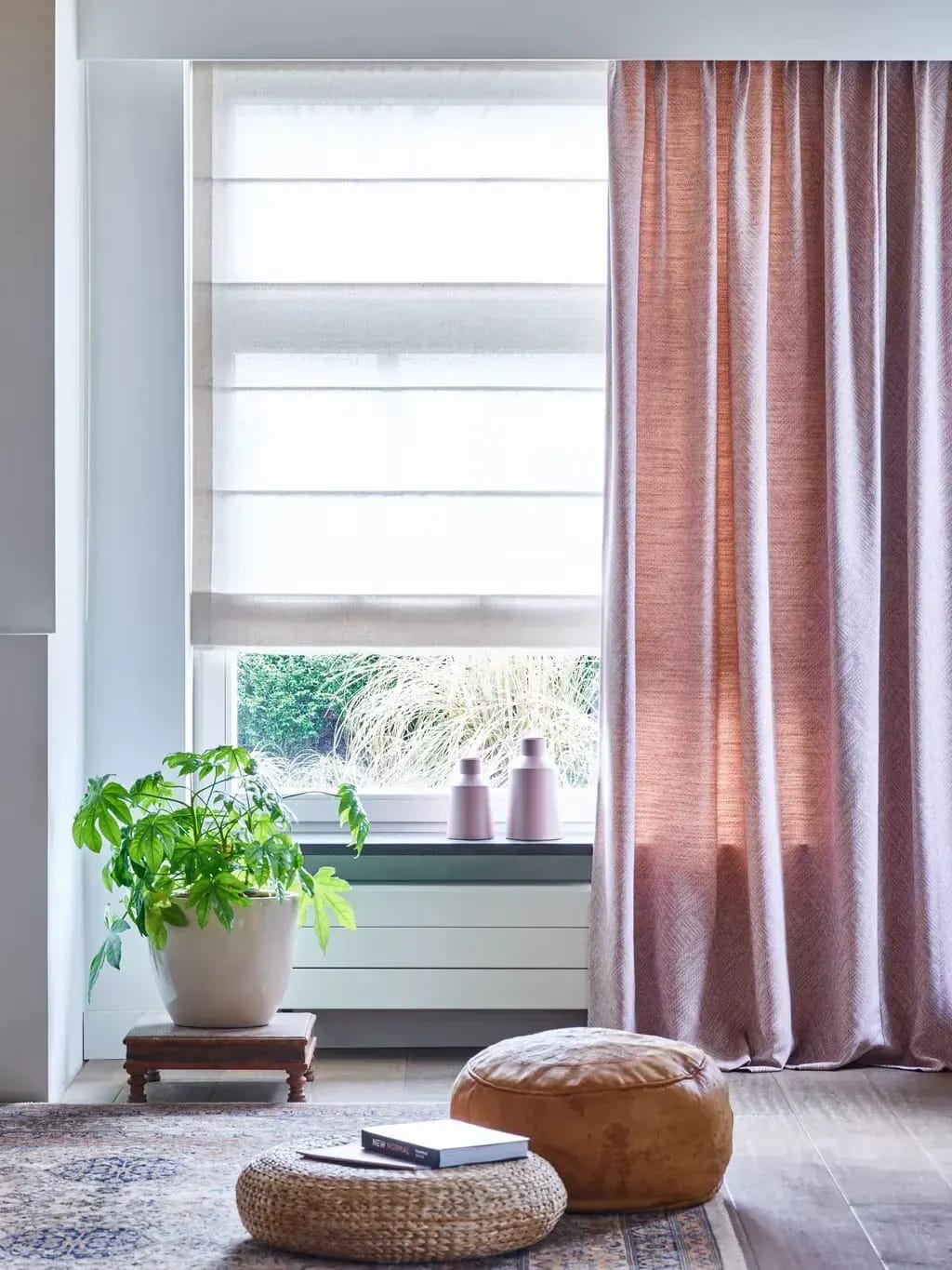 Roze overgordijn en een wit vouwgordijn in een lichte woonkamer.