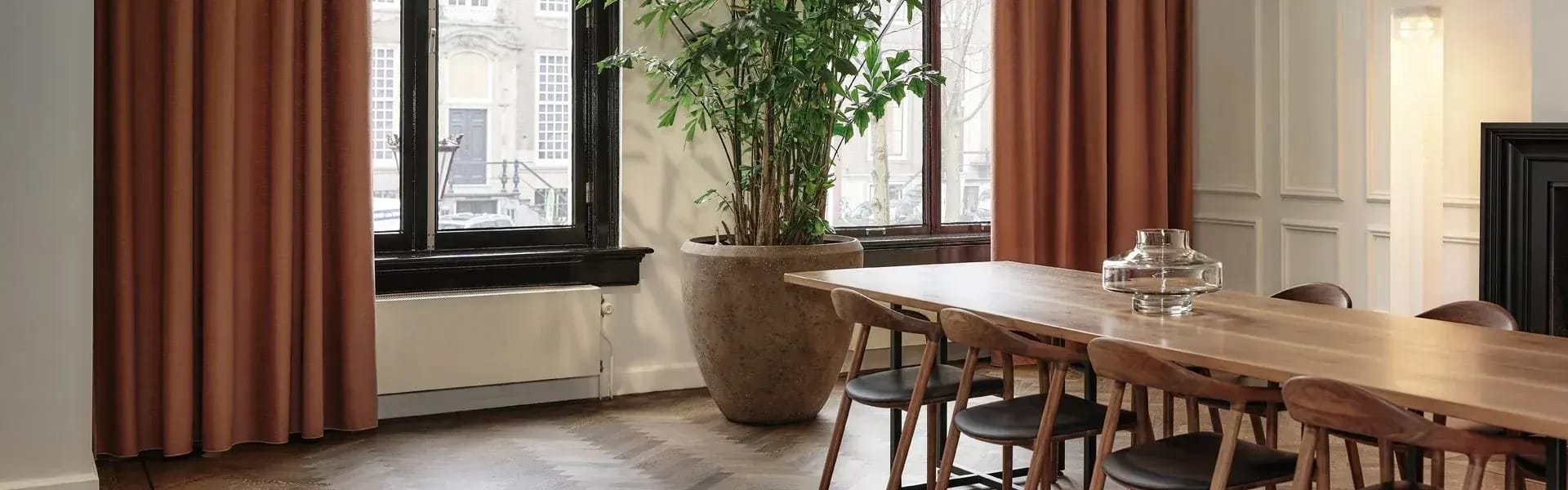 Roestbruine overgordijnen in een eetkamer met een lange houten tafel.