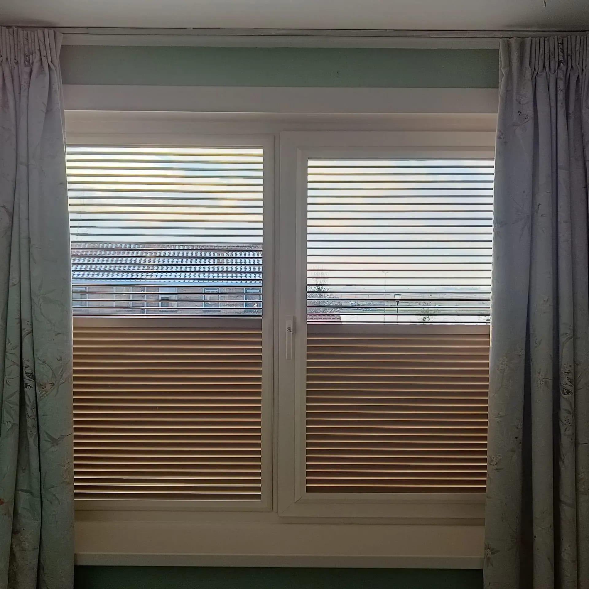 Plisségordijnen die van boven én onder te openen zijn, naast gebloemde overgordijnen.