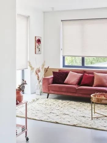 Lichte rolgordijnen in een woonkamer met een roze bank.
