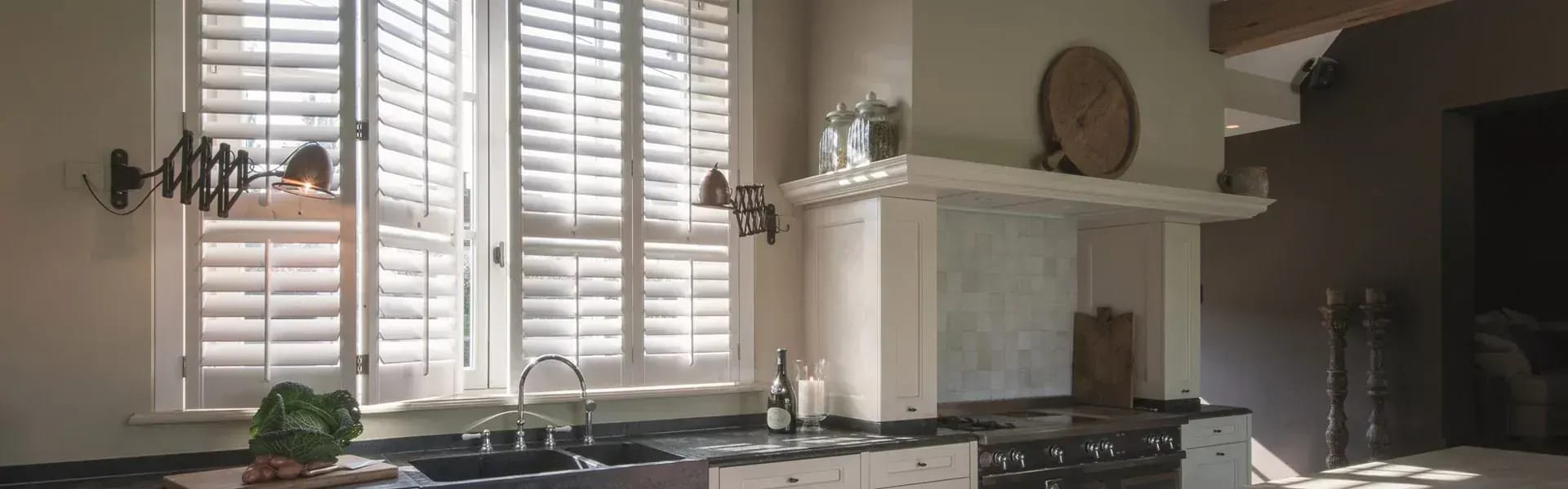 Witte shutters voor de ramen van een landelijke keuken.