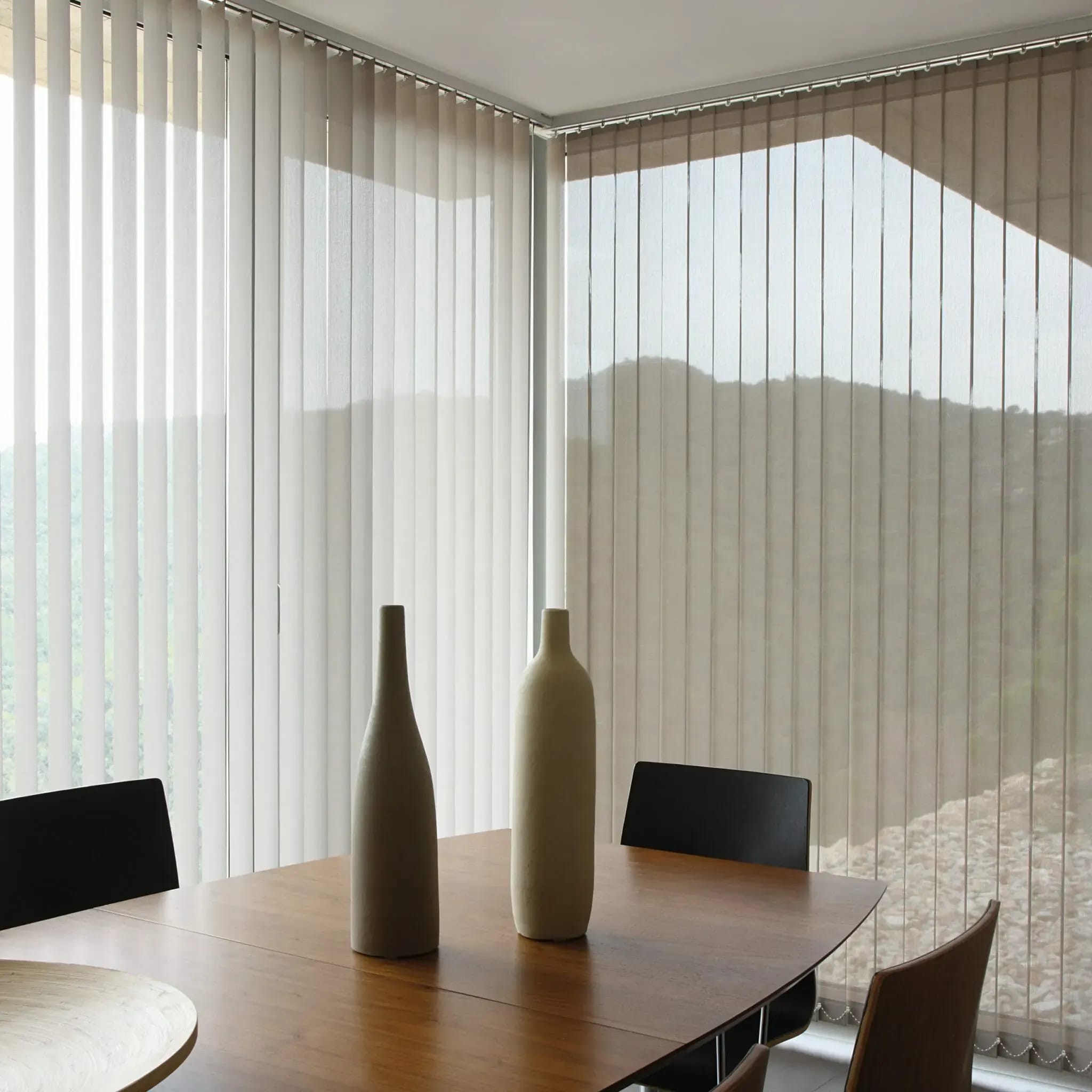 Lichte verticale lamellen achter een eettafel met vazen.