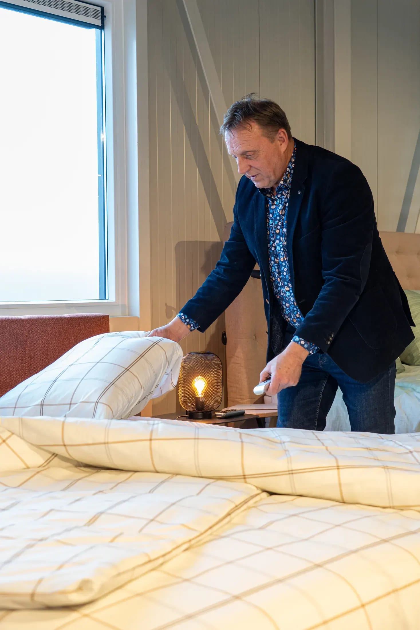 Adviseur schudt een kussen op bij een opgemaakt bed met geruit beddengoed.