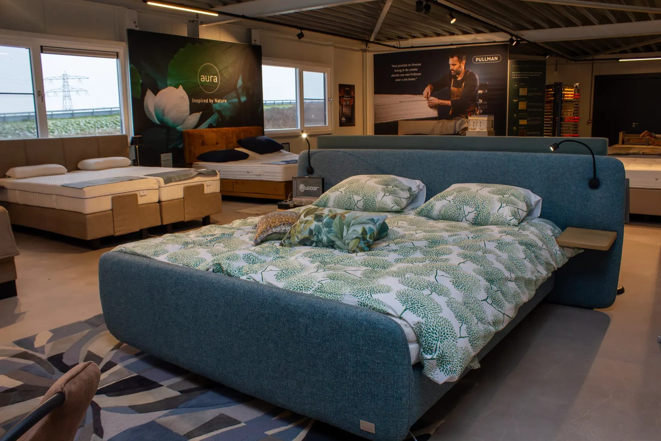 Blauw gestoffeerde boxspring met een dekbedovertrek met groen bladmotief in de slaapafdeling.