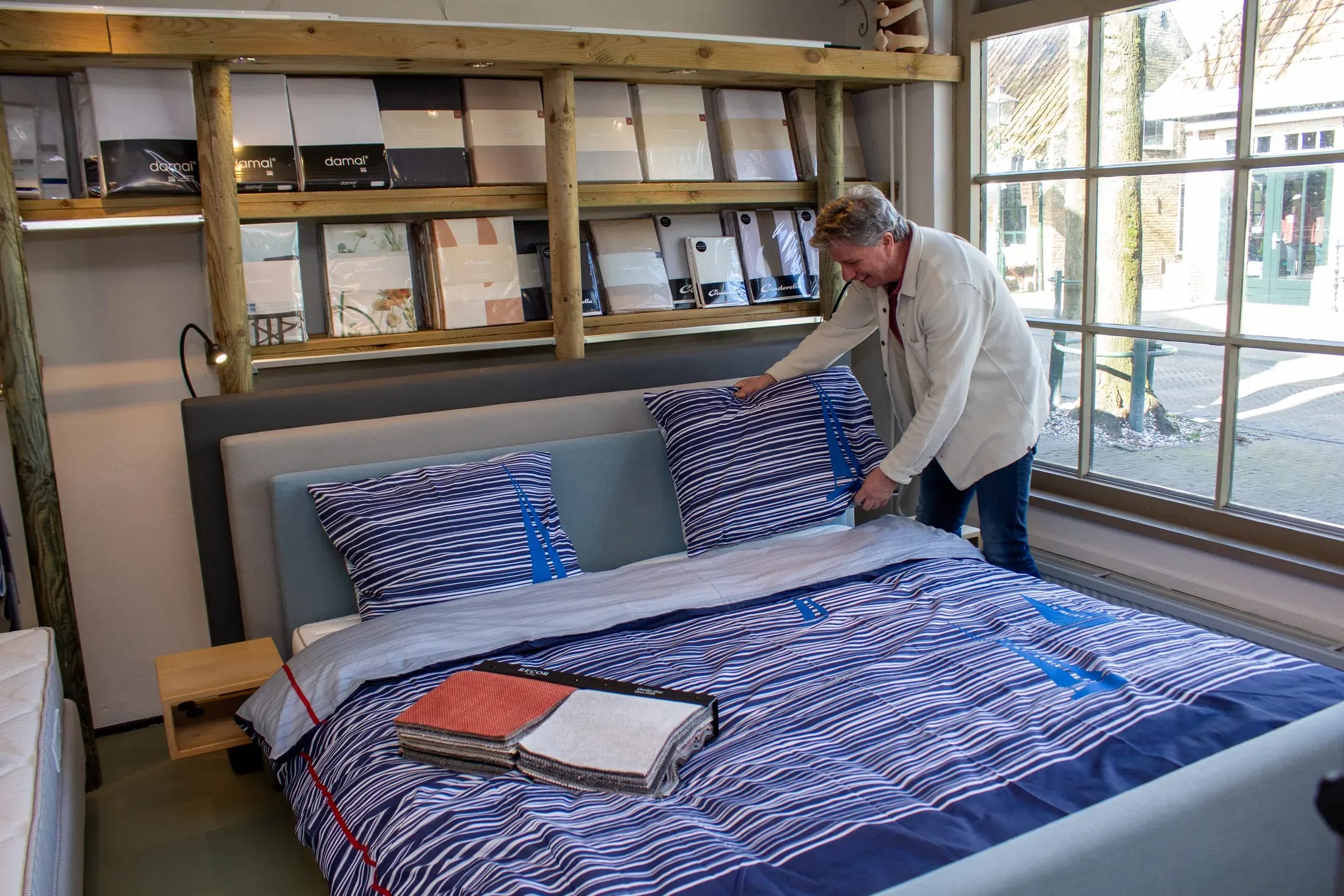 Medewerker maakt een bed op met blauw gestreept beddengoed in de showroom.