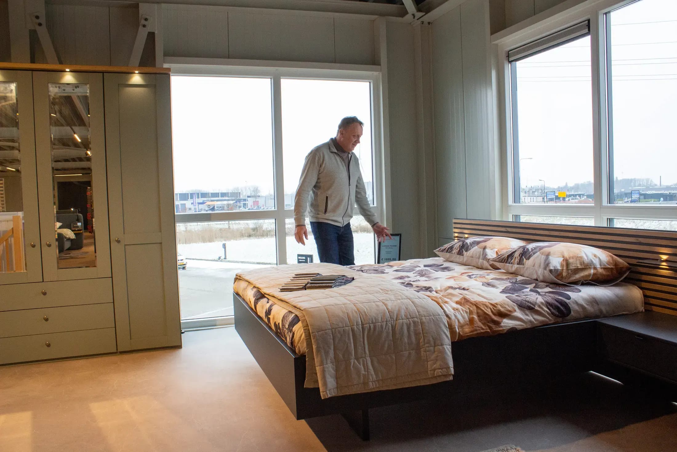 Slaapkameropstelling met linnenkast en bed bij het raam; een medewerker maakt het bed op.