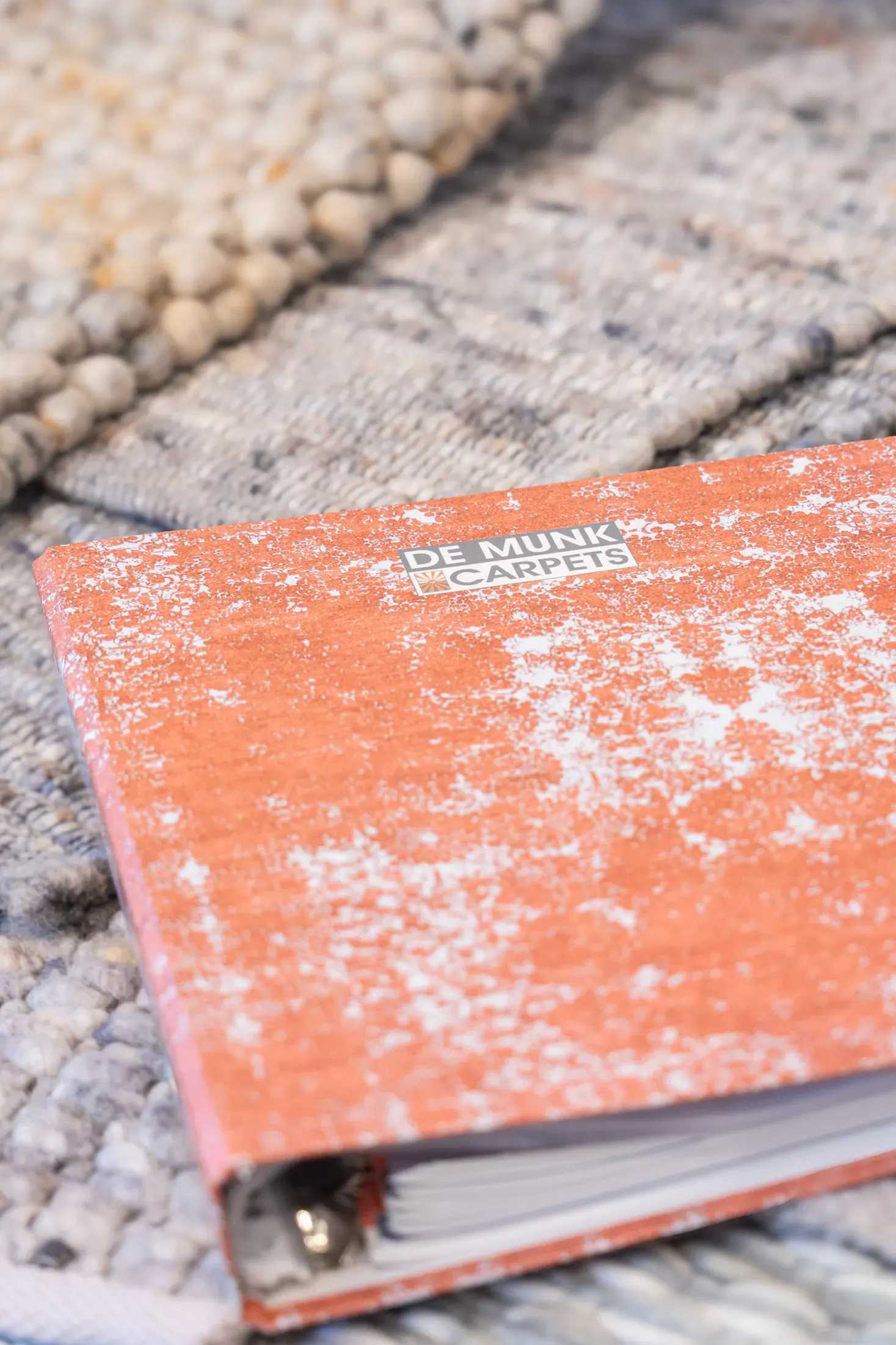 Stalenboek van De Munk Carpets op een gevlochten karpet.