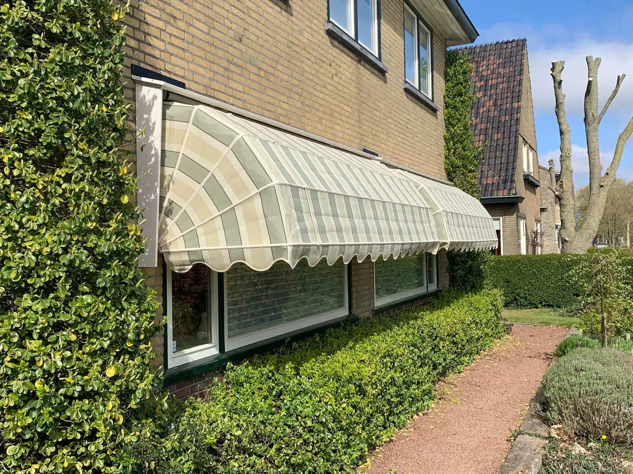 Groen-wit gestreepte markiezen boven de ramen van een bakstenen woning.