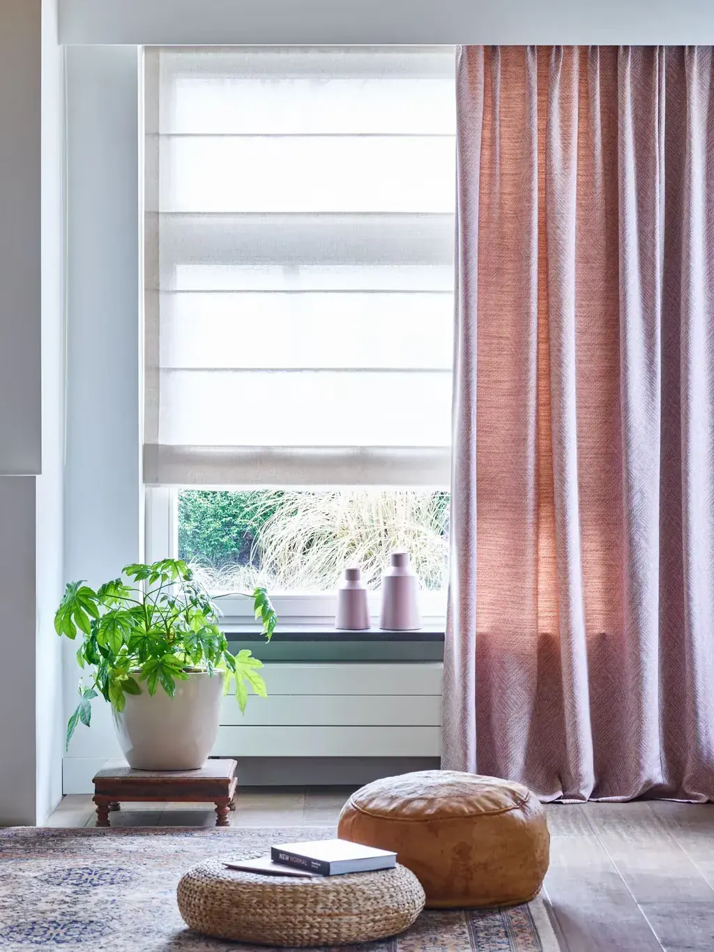 Roze overgordijn en een wit vouwgordijn in een lichte woonkamer.