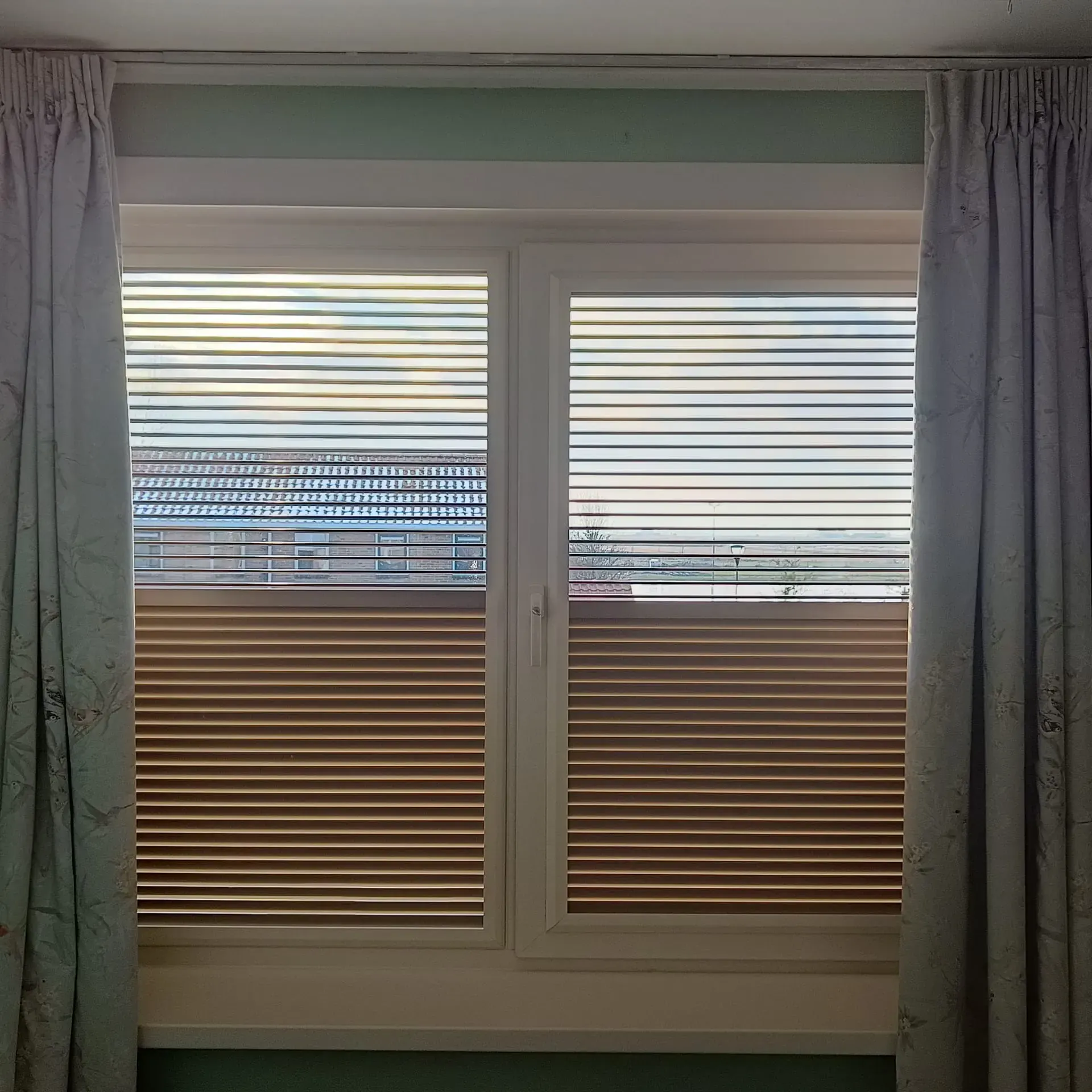 Plisségordijnen die van boven én onder te openen zijn, naast gebloemde overgordijnen.