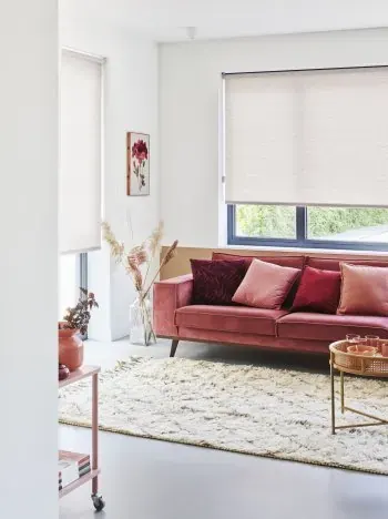 Lichte rolgordijnen in een woonkamer met een roze bank.