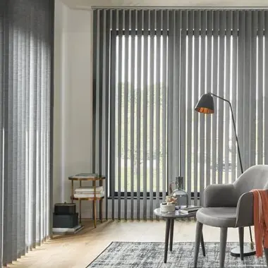 Grijze verticale lamellen in een woonkamer met fauteuil en vloerlamp.