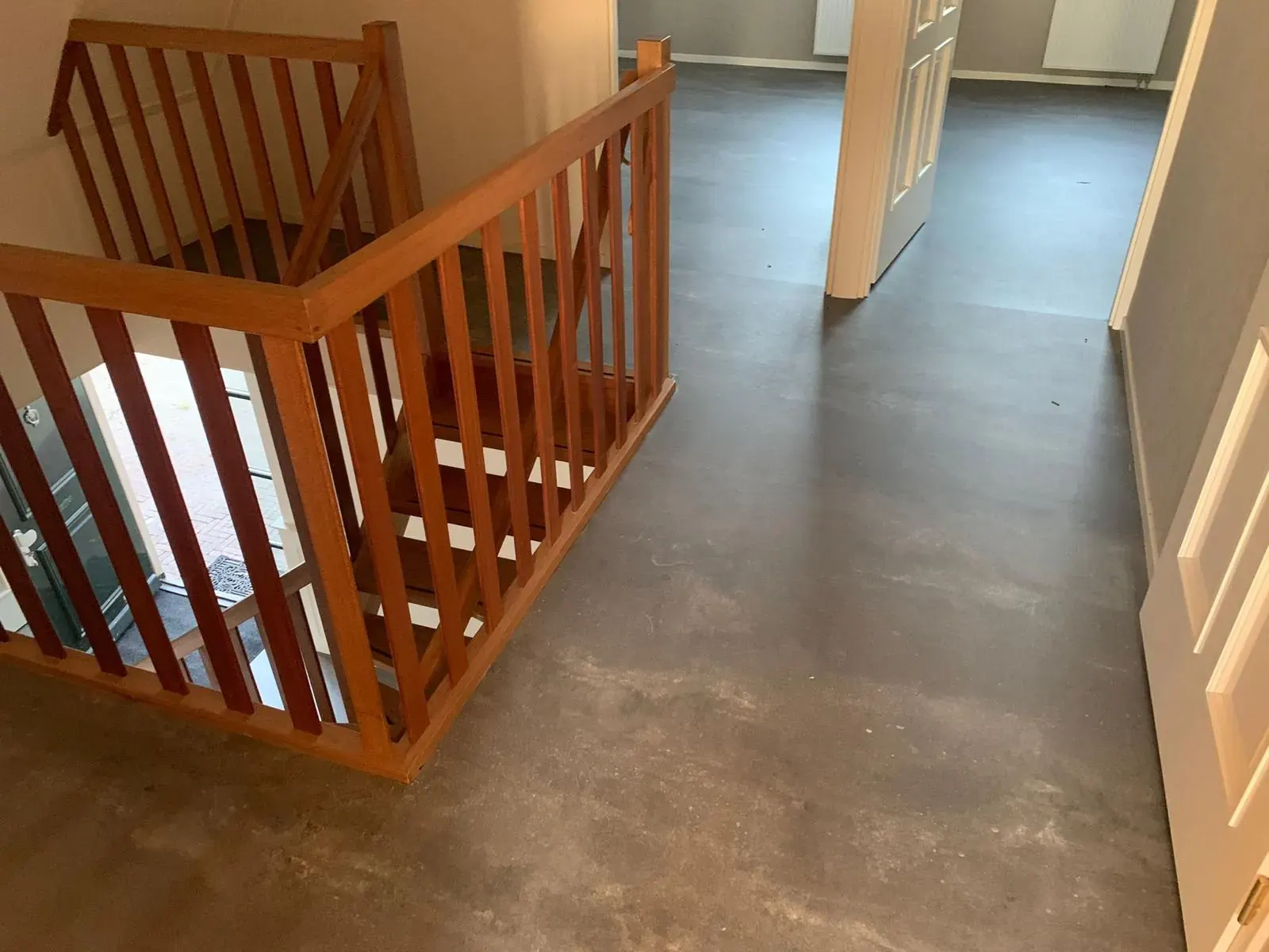 Vinylvloer in betonlook naast een houten trapleuning.